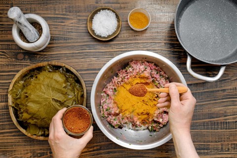 Home cook prepares dolma by adding pepper mix into minced meat. Pickled grape leaves are ready for