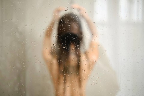 A woman stands in the shower with her hair down, enjoying a peaceful moment. Water cascades down