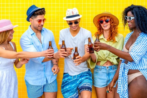 Group of cheerful young friends toasting with beer bottles while standing together against a