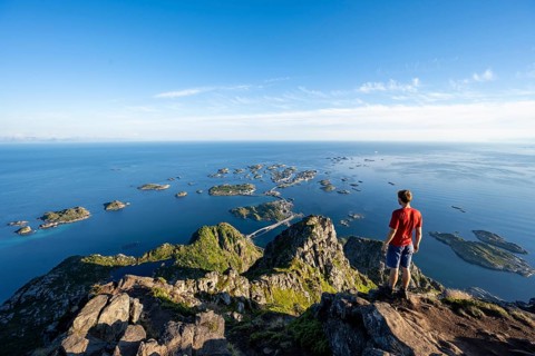View of numerous small rocky islands with houses, mountaineers on the summit of Festvågtind, view