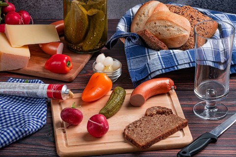 Rustic arrangement with sausage, cheese, vegetables, mustard and bread on a laid table