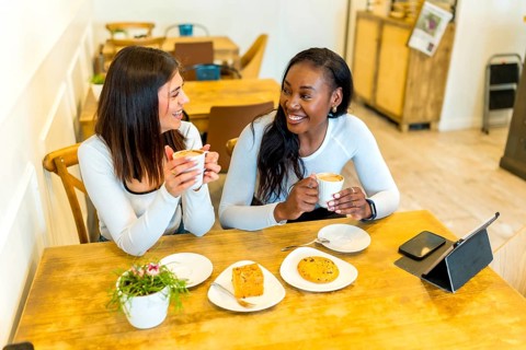 Two female friends enjoying coffee and snacks while chatting and laughing together at a cozy cafe