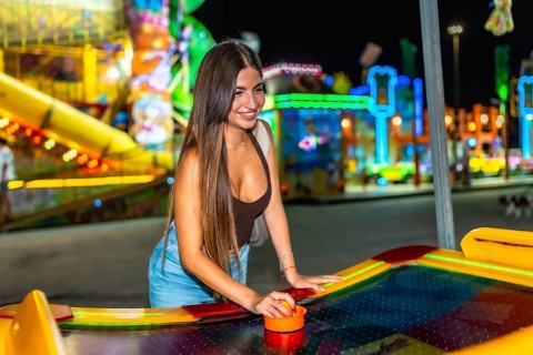 Happy woman playing air hockey at amusement park, enjoying nightlife entertainment with colorful