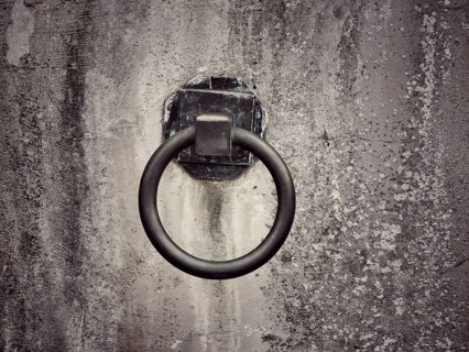 A weathered wall features a rusty metal ring affixed to it, suggesting a historical purpose. The