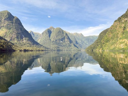 Mountains with reflections in the water against a blue sky in Doubtful Sound, South Island, New