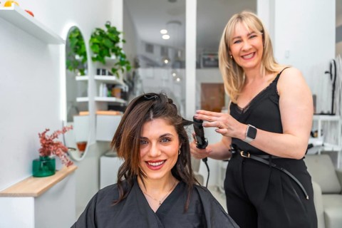 Smiling hairdresser styling hair of female customer with a curling iron in a modern, vibrant hair