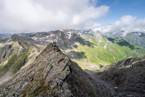 Mountaineer on a steep rocky ridge, on the summit of the Lasörling, view of the mountain panorama