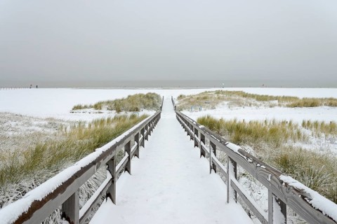 Winter day, onset of winter, wooden plank path leads through the snow-covered dune landscape to the