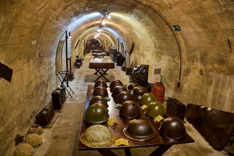 A tunnel with historical helmets displayed on a table, illuminated by warm light, steel helmets,