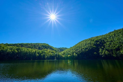 Bright sun over a calm lake with green hills and blue sky, summer, Rursee, Obersee, Simmerath,
