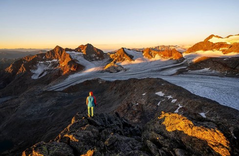 Mountaineer in front of picturesque high mountain landscape at sunrise with alpenglow, glacier and
