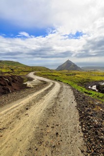 Gravel track through barren moss-covered volcanic landscape, cone-shaped mountain Stapafell, rain