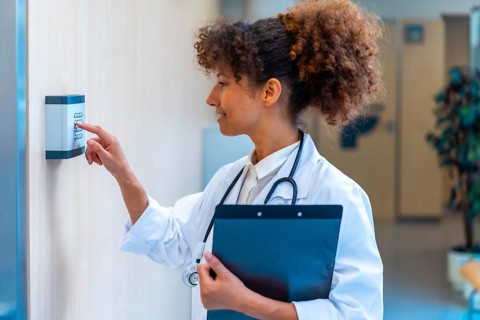 Confident female doctor using a keypad to enter a code, holding a clipboard in a hospital corridor