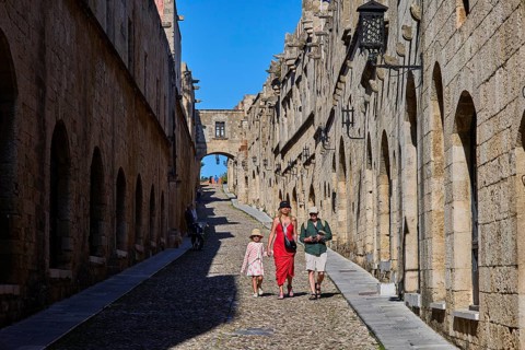Tourists walking through a sunny, stony alley, Knights Street, Rhodes Old Town, Rhodes, Dodecanese,