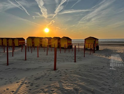 Beach huts at sunset with sand and sea in the background. The sky is streaked with clouds, De