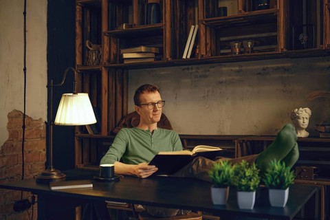 A person sits comfortably in a modern workspace, immersed in a book. Soft lamp light creates a warm
