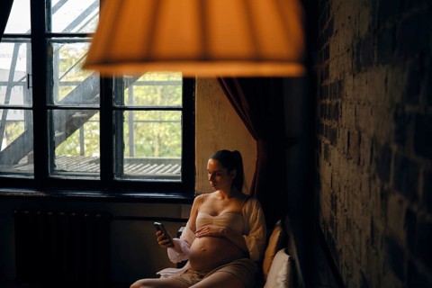 In a cozy room filled with natural light, a pregnant woman sits comfortably on sofa and making