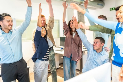 Multicultural businesspeople celebrating success in a bright office, raising arms in unity,