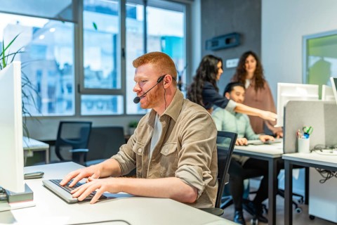 Focused call center agent providing customer support, typing on keyboard while wearing headset in