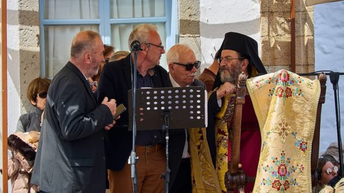 Several men, including priests, discussing in front of a crowd, one holding a microphone,