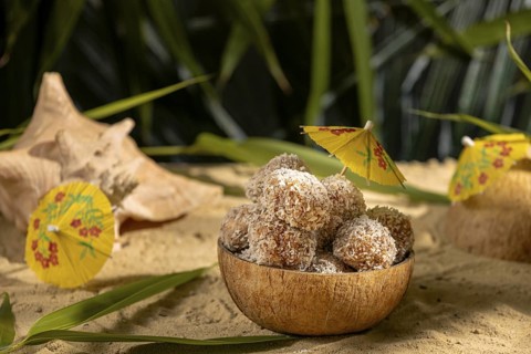 Coconut, bowl filled with sweet confectionery on sand, decorated with yellow umbrellas