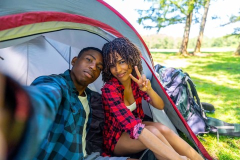Young couple taking a selfie inside their tent while camping in nature, enjoying a relaxing