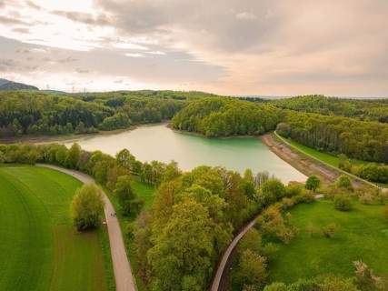 Spring in nature with a forest lake and paths under a cloudy sky, Glems reservoir, Swabian Alb,