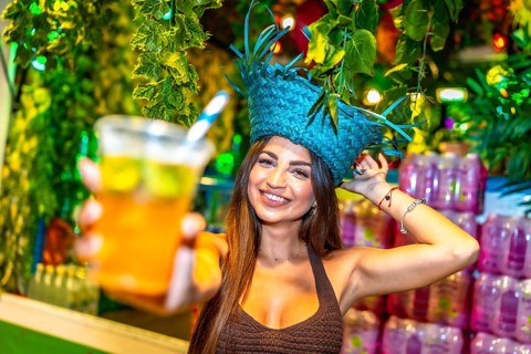 Smiling bartender wearing a straw hat offering a refreshing tropical cocktail at a vibrant tiki