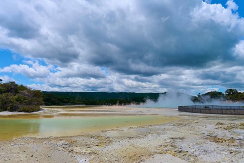 Vapour emissions from a geothermal area under a cloudy sky, surrounded by nature and trees,