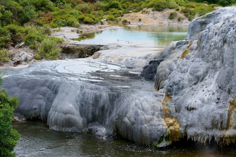 White mineral deposits and rock formations surround a geothermal spring with clear water and dense