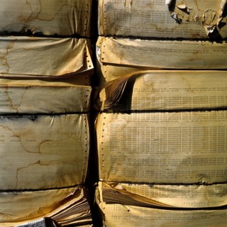 A large stack of compressed paper products is arranged in a recycling area. The paper displays wear