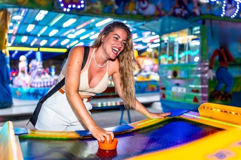 Cheerful young woman laughing and enjoying a lively game of air hockey at a vibrant amusement park,