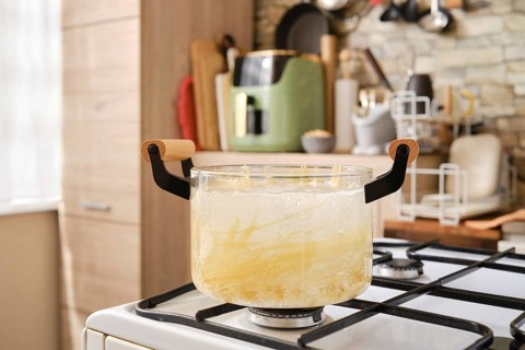 A glass pot filled with boiling water and pasta on a stovetop in a contemporary kitchen. The cozy