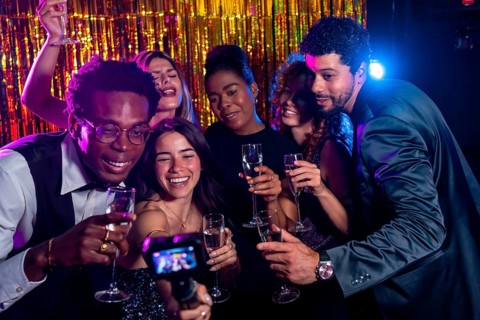 Group of cheerful multi ethnic friends taking selfie with action camera while enjoying champagne