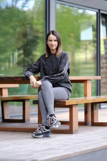 A young woman is seated at a wooden table outdoors, dressed in comfortable athletic wear. She