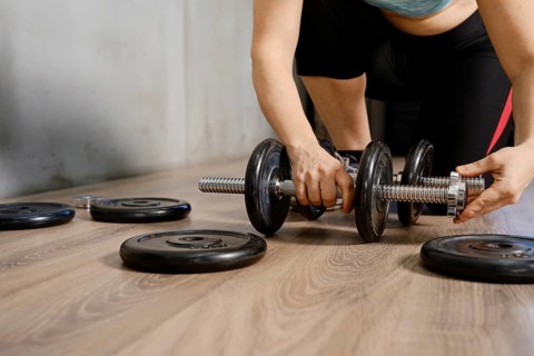 A person is adjusting weights on a dumbbell while preparing for an intense workout. The setting is