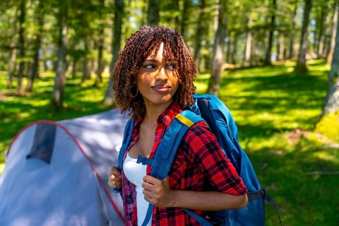 Young woman with a backpack enjoying the tranquility of a forest, discovering nature while camping