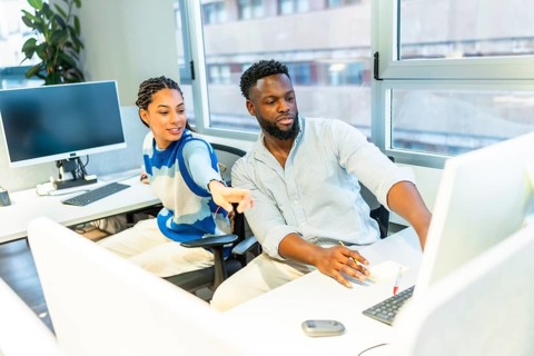 Two colleagues are working together in a modern office, discussing a project on a computer,
