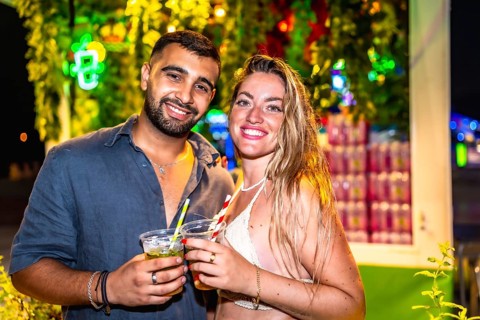 Young man and woman enjoying cocktails at a vibrant night market, celebrating summer with