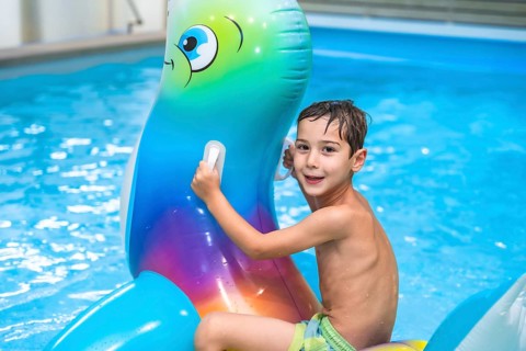Smiling boy having fun riding an inflatable toy whale in a home swimming pool, enjoying summer