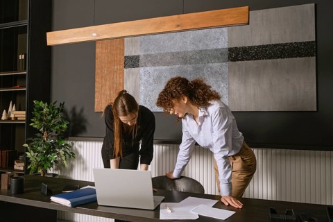 Two women discuss a project at a contemporary office desk, engaging with a laptop and scattered