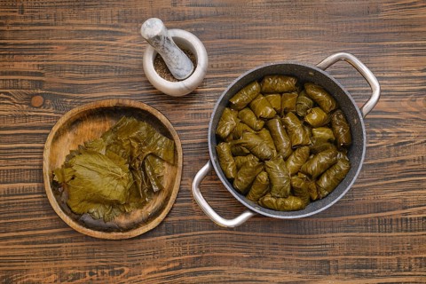 Delicious dolma is being prepared at home, featuring grape leaves wrapped around a savory filling.
