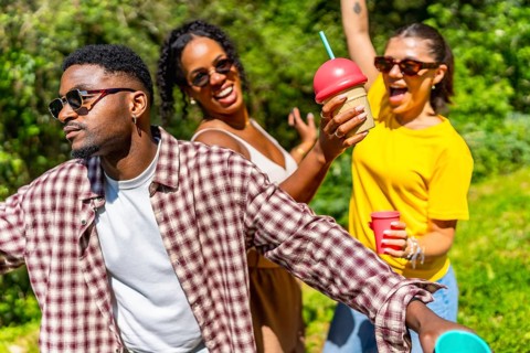 Three friends enjoying summer sunshine, dancing joyfully while sipping cold drinks and sharing
