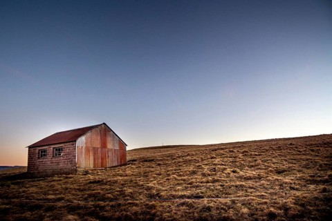 An isolated wooden hut sits on a grassy slope in the Regional Nature Park of Volcans d'Auvergne,