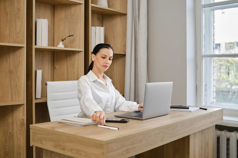 A businesswoman working at a desk with a laptop reached for a pen to make a note