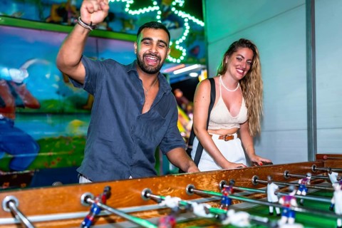 Young man and woman enjoying a foosball game at a funfair, celebrating a goal with excitement and