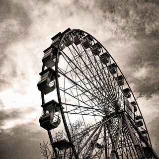 A towering Ferris wheel emerges against a swirling, moody sky during twilight hours, evoking