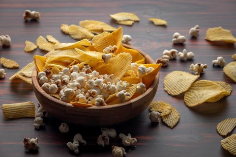 Wooden bowl with crisps and popcorn scattered on the table