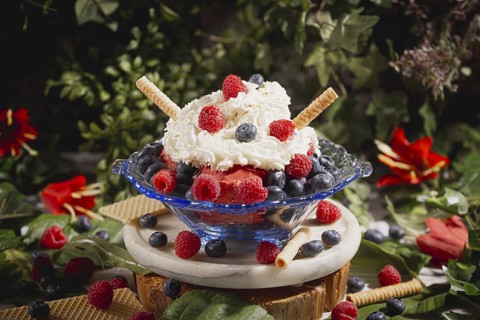 Colourful sundae with raspberries and blueberries, decorated with cream and waffle, surrounded by