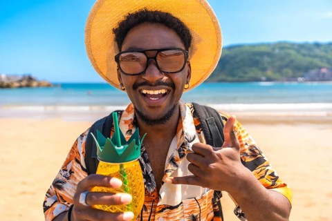 Young man enjoying summer vacation on a tropical beach, holding a pineapple shaped cocktail and